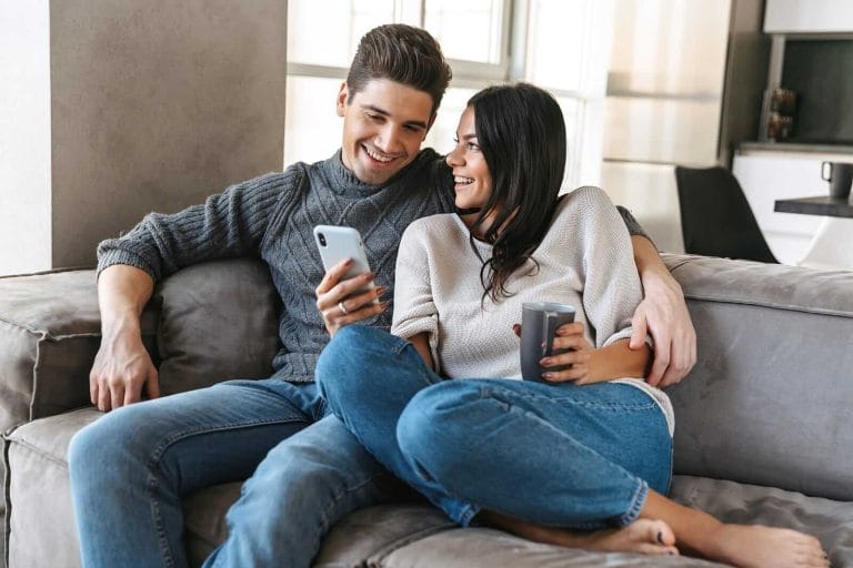 Happy young couple sitting on a couch at home, drinking tea, loo