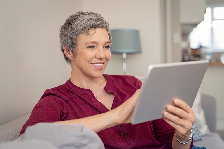 Smiling senior woman looking her digital tablet while sitting on