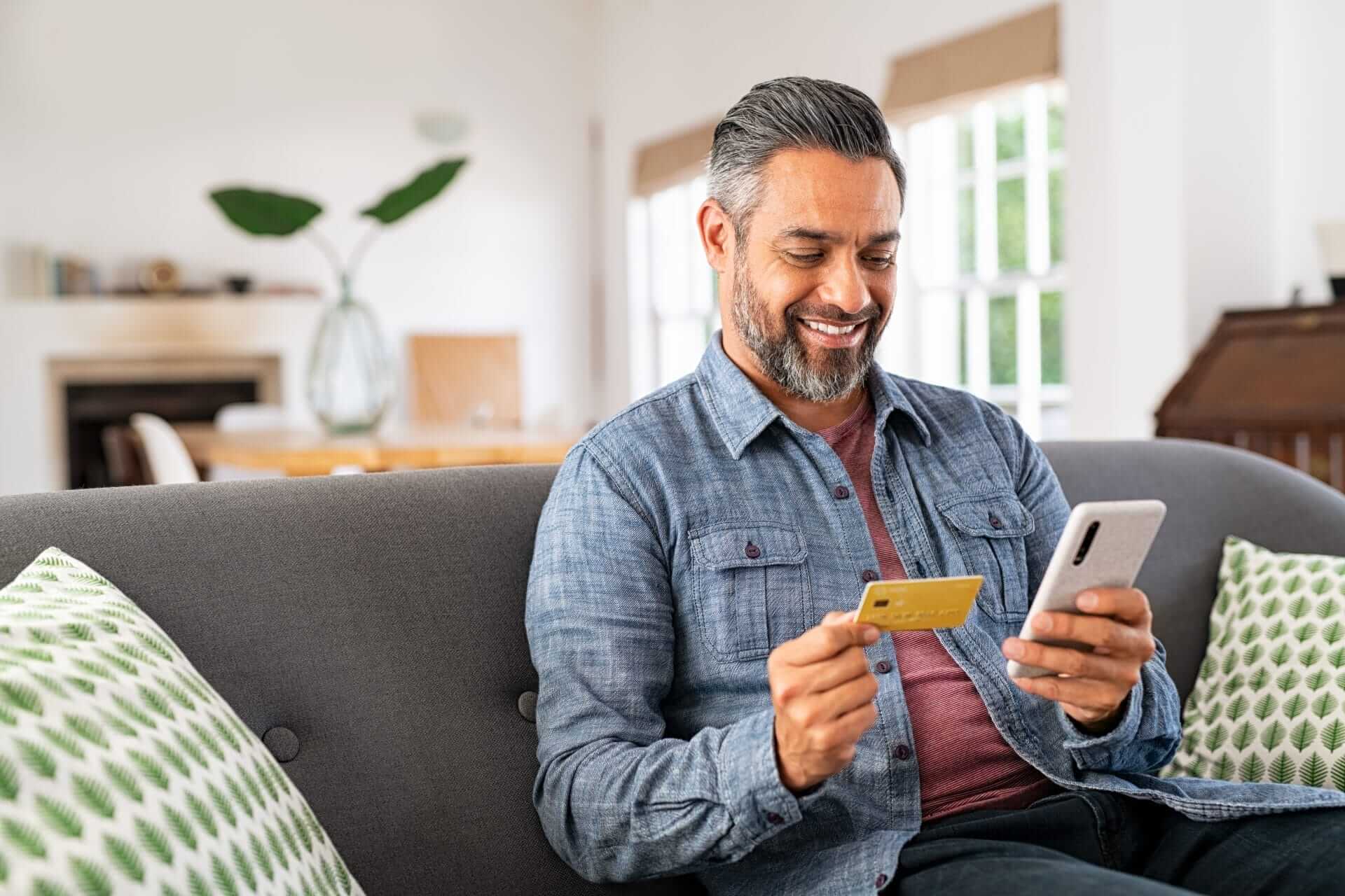 smiling, Mature man looking at phone and credit card while in the living room